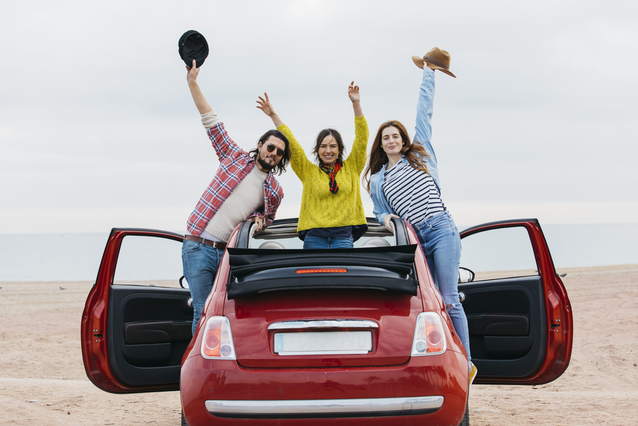 smiling-women-near-man-with-upped-hands-leaning-out-from-car-shore